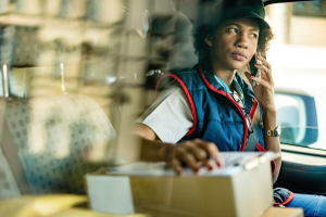 african-american-delivery-woman-talking-with-customer-mobile-phone-while-sitting-mini-van-view-is-through-window_637285-1248